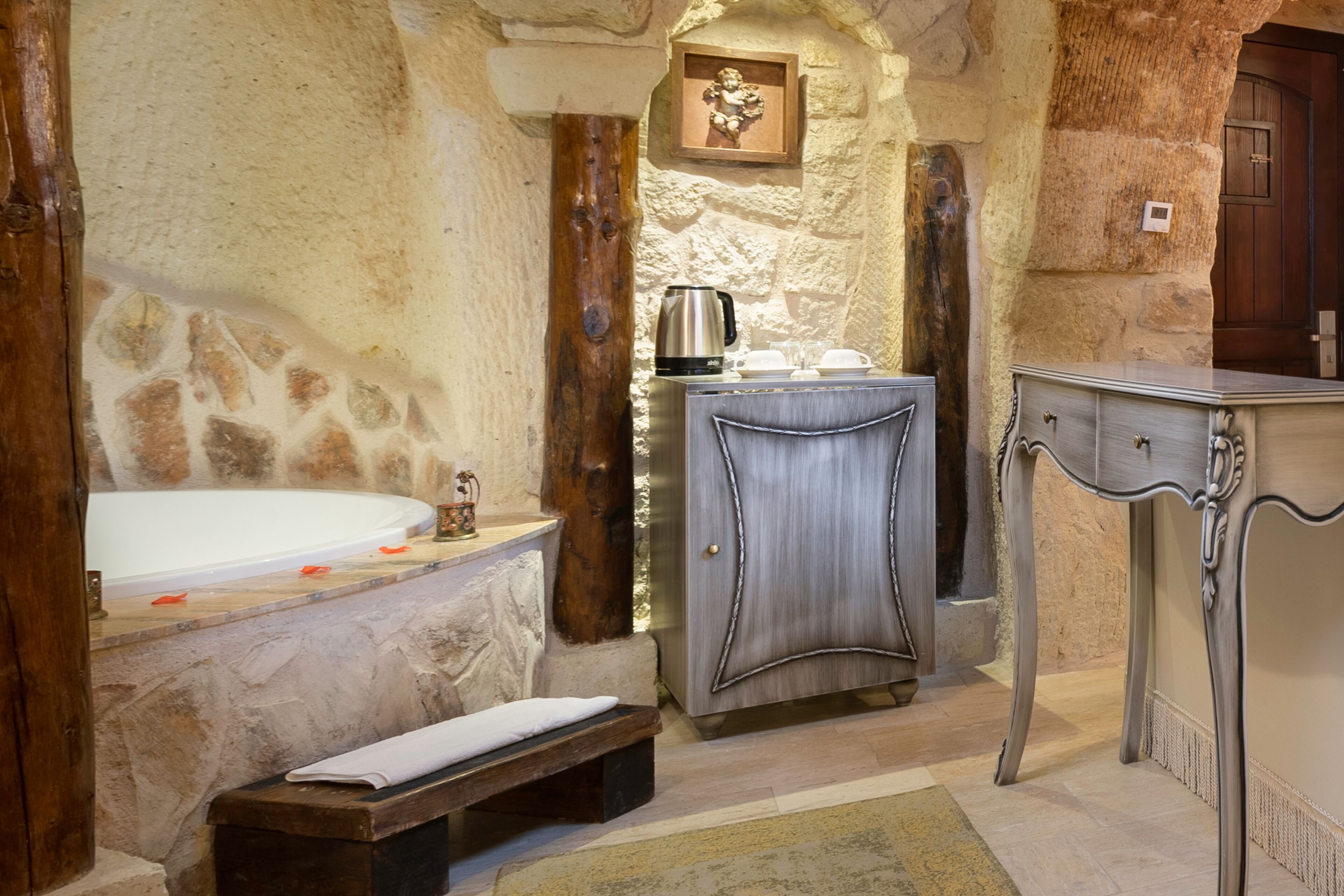 A stone-walled bathroom with a bathtub, a wooden bench, a sink, and a cabinet.