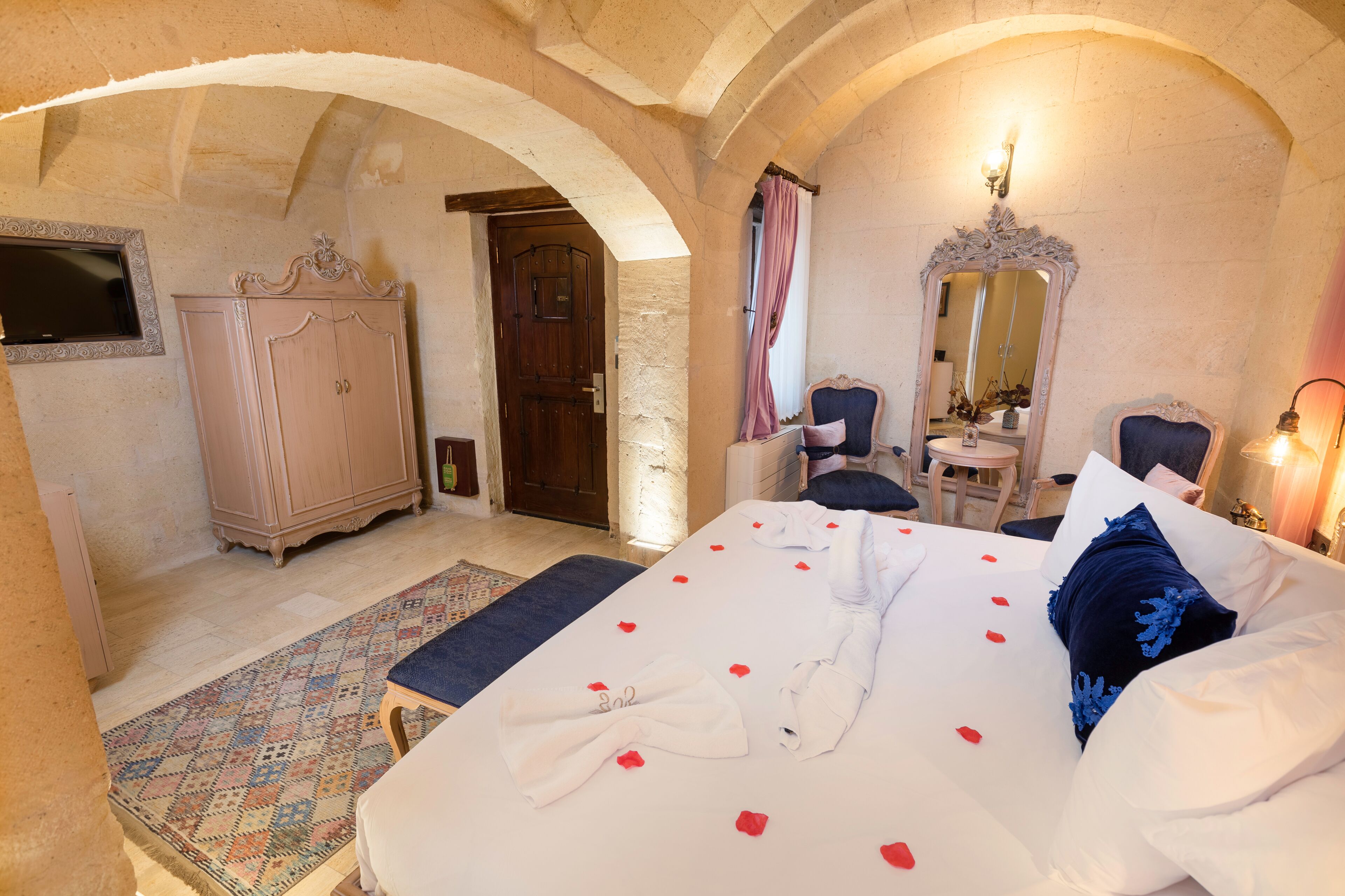 A bedroom with a large bed, a wardrobe, a mirror, and a small table.