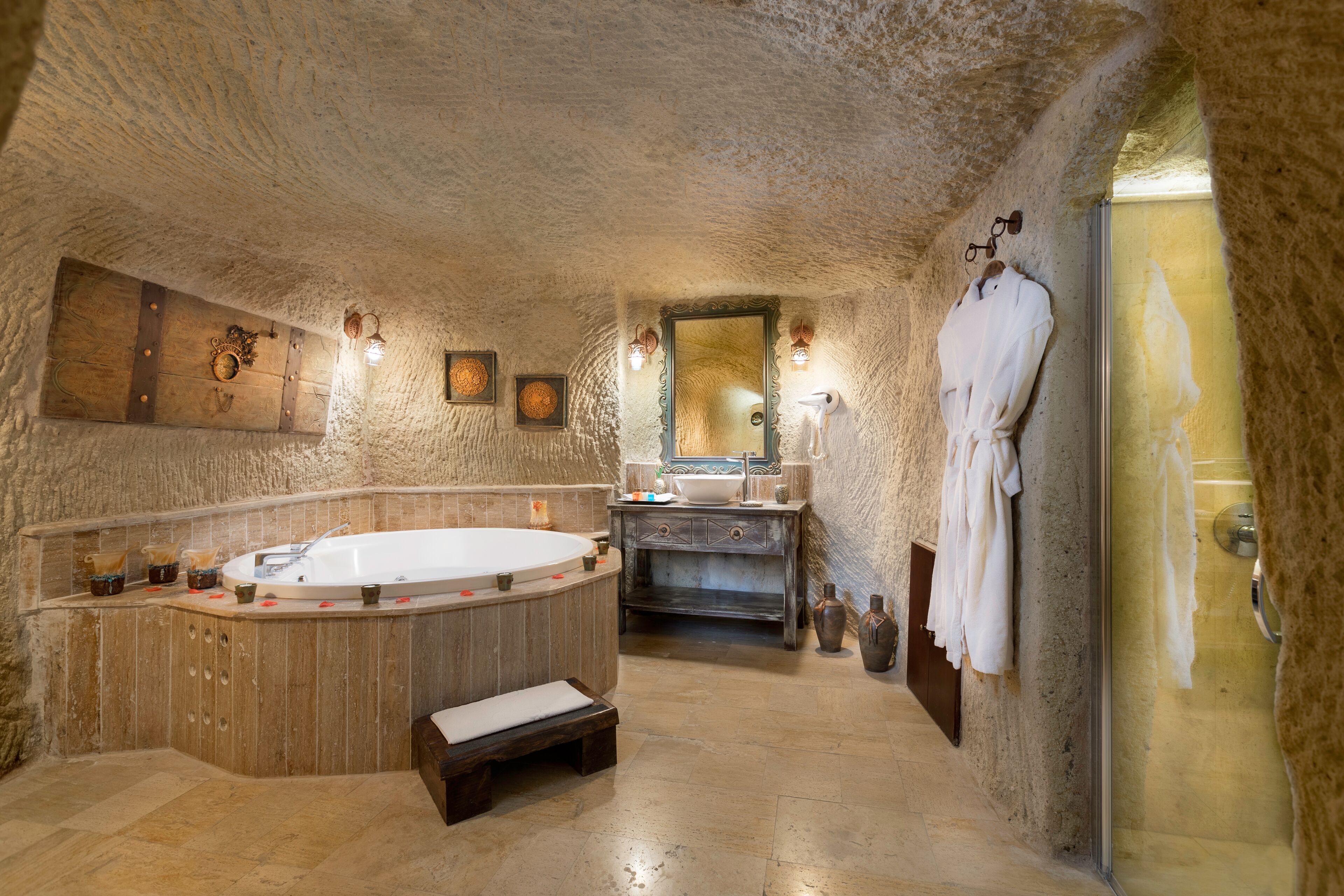 A stone-walled bathroom with a freestanding bathtub, a vanity with a mirror, and a robe hanging on the wall.