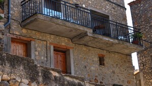 A stone building with a balcony, wooden doors, and a stone wall. - Casa amb vistes al Pallars Jussà (Conca de dalt)
