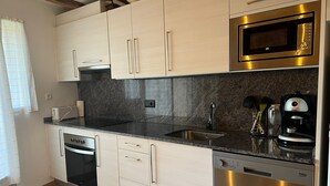 A modern kitchen with light wood cabinets, a black countertop, stainless steel appliances including a microwave, oven, and dishwasher, and a granite backsplash. - Casa amb vistes al Pallars Jussà (Conca de dalt)