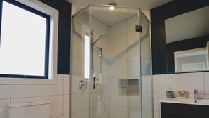 Uma casa de banho moderna com chuveiro com divisória de vidro, sanita e lavatório com espelho em cima.