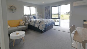 Quarto com cama, sofá, mesa pequena e porta de vidro deslizante para área externa.