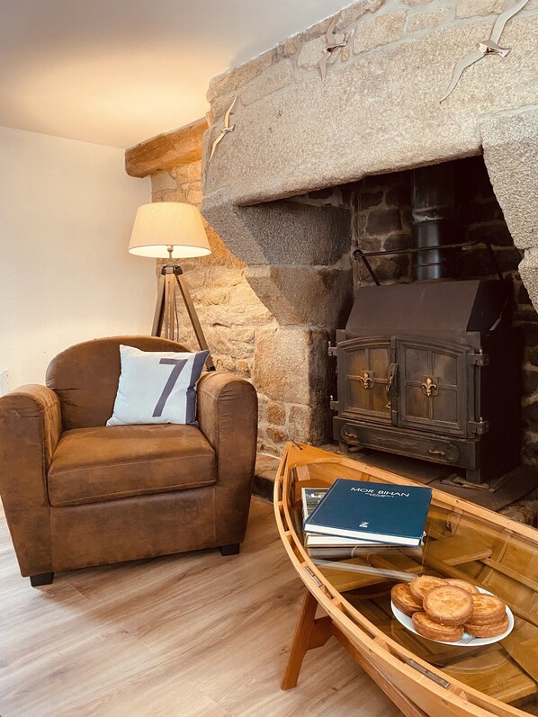 Un salón acogedor con chimenea de piedra, un sillón de cuero marrón, una lámpara y una bandeja con pasteles.