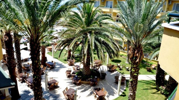 A courtyard with palm trees, outdoor seating, and a building in the background. - Varol Otel (Ayvalik)