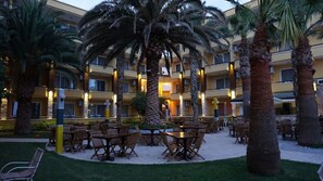 A hotel courtyard with outdoor seating, palm trees, and a building with multiple balconies.