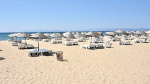 A beach with rows of white lounge chairs and thatched umbrellas. - Varol Otel (Ayvalik)