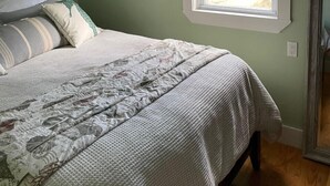 A bedroom with a bed, a window with a patterned valance, a wall clock, and a framed picture.