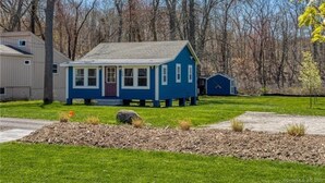 A blue house with a front porch, a shed, and a yard with a small rock garden.