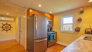 A kitchen with wooden cabinets, stainless steel appliances, a ship's wheel decoration, and a window with a city view.