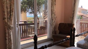 A balcony with a wooden chair, a cushioned bench, and a view of trees and buildings. - Spacious Villa for 10, 100m from Beach, WiFi, Garden, A/C, Near Shops, Parking Available (Le Barcarès)
