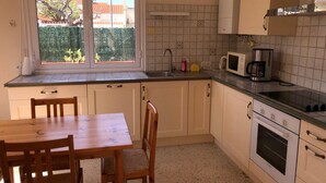 A kitchen with a dining table, chairs, a microwave, a coffee maker, and a window with a view of greenery. - Spacious Villa for 10, 100m from Beach, WiFi, Garden, A/C, Near Shops, Parking Available (Le Barcarès)