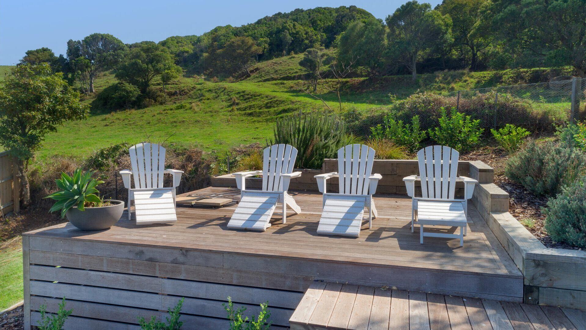 Una terraza con sillas Adirondack blancas y una planta en maceta.