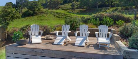 Una terraza con sillas Adirondack blancas y una planta en maceta.