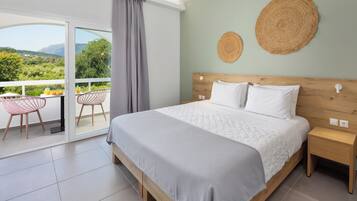 A bedroom with a large bed, a nightstand, a wooden headboard, two woven wall decorations, and a balcony with chairs and a table.