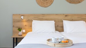 A neatly made bed with white linens, a bedside table with a vase of flowers, and a tray with oranges and cups. - La Maison Corfu - Adults Only (Corfu)