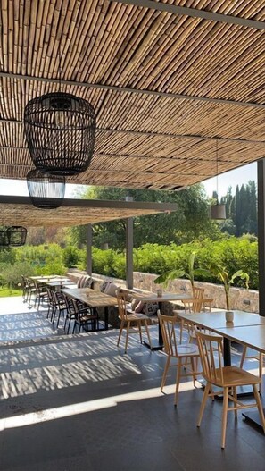 Un espace de restauration en plein air doté d’un plafond en bambou, de murs en pierre et offrant une vue sur la verdure.