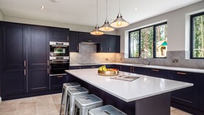 A modern kitchen with dark cabinetry, stainless steel appliances, and a large island with stools. - Broad House  - sleeps 8 guests  in 4 bedrooms (Dilham)