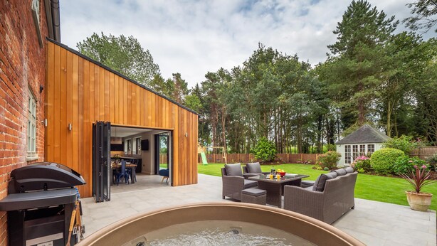 A backyard with a hot tub, outdoor seating, a wooden deck, and a play area. - Broad House  - sleeps 8 guests  in 4 bedrooms (Dilham)