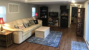 Uma sala de estar com um sofá bege, uma mesa de centro, uma estante de livros e uma televisão.