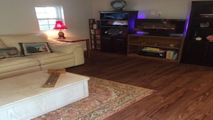 Uma sala de estar com um sofá, uma mesa de centro, uma estante de livros e uma televisão.