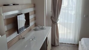 A hotel room with a flat-screen TV, a desk with a cup and glasses, a bed, and a window with curtains. - Otel Bostanci (Izmit)