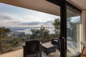 Enjoy the breathtaking view of the coastal landscape from this balcony, featuring a body of water, distant mountains, and a town below.