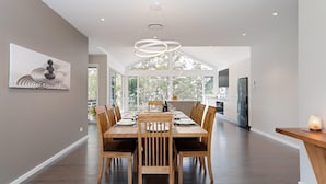 A modern kitchen with a dining area, featuring a large window, a pendant light, and a minimalist design. - Iluka, 46 Soldiers Point Rd - Stunning Air Conditioned house with WIFI & Water Views (Soldiers Point)