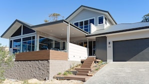 A modern two-story house with large windows, a stone retaining wall, and a garage. - Iluka, 46 Soldiers Point Rd - Stunning Air Conditioned house with WIFI & Water Views (Soldiers Point)
