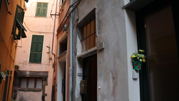 A narrow street with buildings, a visible door, and a small window with a flower box.