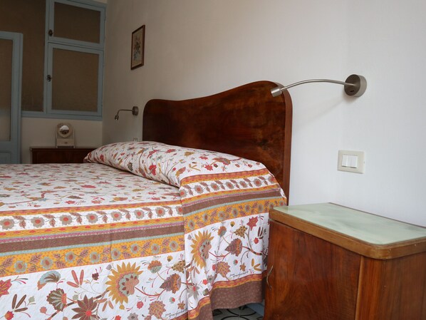 A bedroom with a wooden headboard, a floral bedspread, a bedside table, and a wall-mounted lamp. - Casa Gigio Vernazza Cinque Terre (Vernazza)