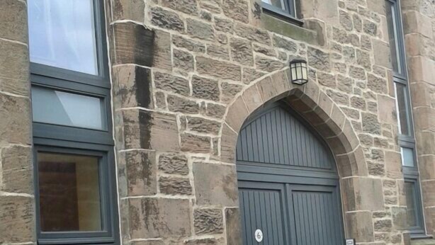 Un bâtiment en pierre doté d’une grande entrée en arc de cercle et d’une enseigne portant le chiffre « 6 » au-dessus de la porte.