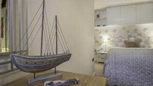 Une maquette de bateau sur une table, un lit avec une literie à motifs floraux et une table de chevet avec une lampe.