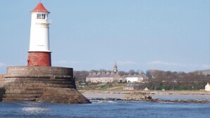 Un phare perché sur un promontoire rocheux, d’où l’on a une vue dégagée sur une ville et une église en arrière-plan.