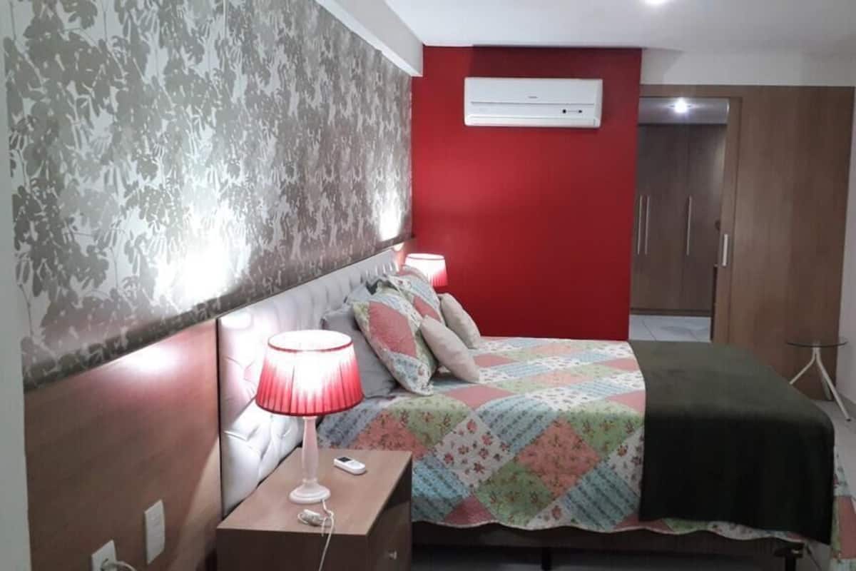 Un dormitorio con cama, mesita de noche con lámpara, aire acondicionado de pared y armario.