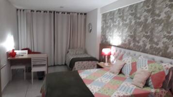 Quarto de hotel com duas camas, uma escrivaninha, uma cadeira e um abajur.