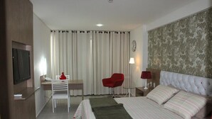 A hotel room with a bed, a desk with a chair, a TV, and a window with curtains. - Betel Beach Flat (Recife)