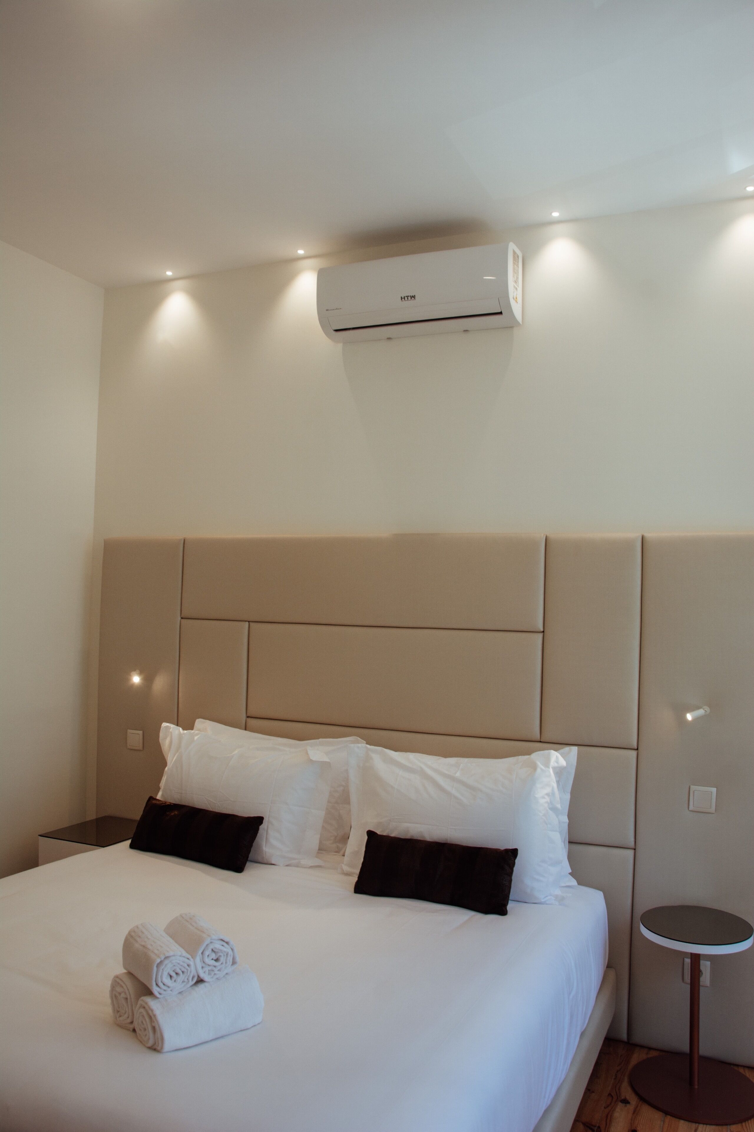 Habitación de hotel con una cama grande, ropa de cama blanca, una mesa redonda y un equipo de aire acondicionado en la pared.