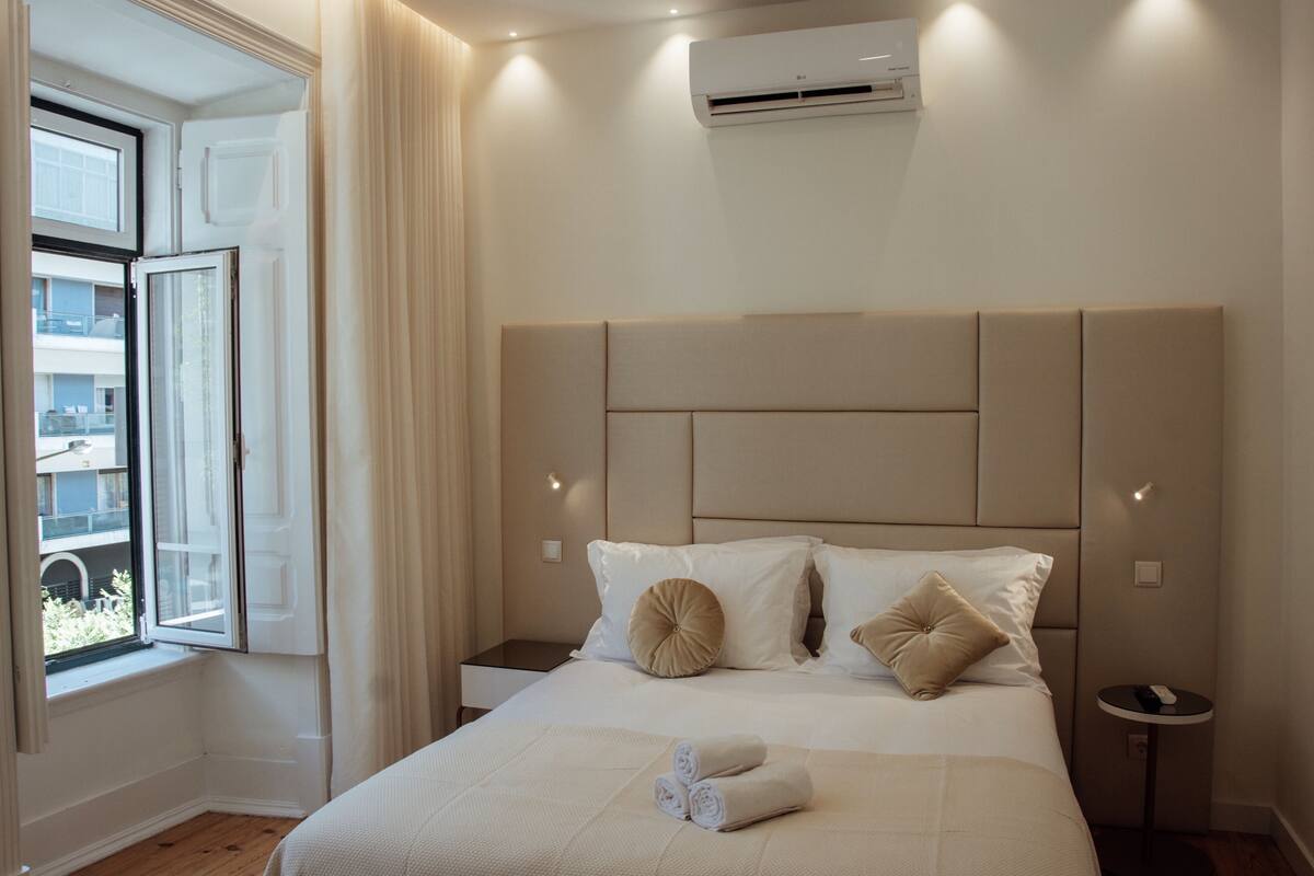 Ein Hotelzimmer mit einem großen Bett, einem fensterbelaubten Fenster, einer Klimaanlage und einem kleinen Nachttisch.