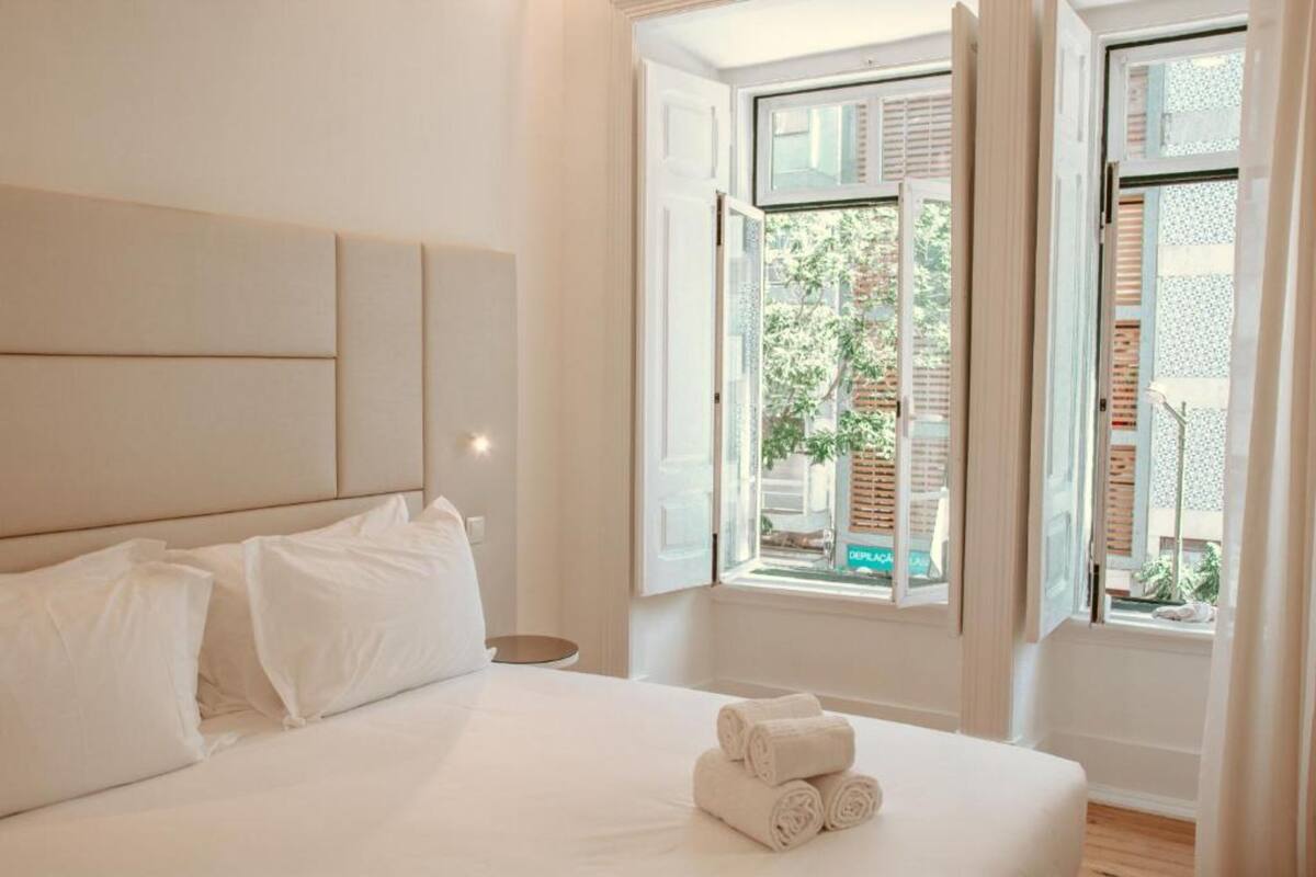 Ein Hotelzimmer mit Bett, Kissen, Nachttisch und Fenster mit Blick nach außen.