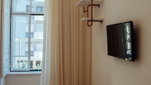 A hotel room with a bed, a desk, a chair, a TV mounted on the wall, and a window with curtains. - Le Premier Lisbon Suites (Lisbon)