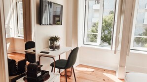A modern room with a white desk, a black chair, a coffee machine, and a TV mounted on the wall. - Le Premier Lisbon Suites (Lisbon)