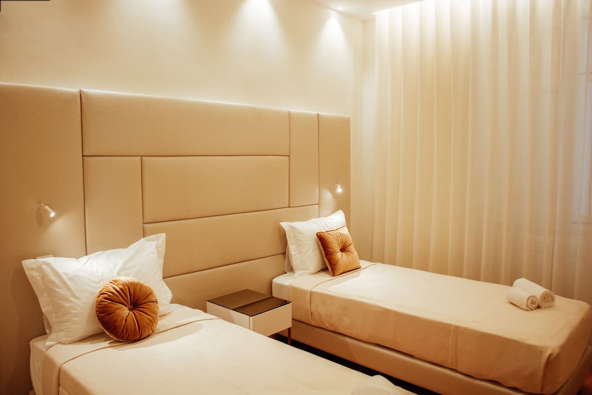 Ein Hotelzimmer mit zwei Betten, einem Kopfteil, einem Nachttisch und einem Fenster mit Jalousien.