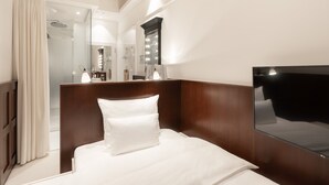 Une chambre d’hôtel équipée d’un lit, d’un grand miroir, d’un téléviseur à écran plat et d’une salle de bain visible à travers une porte en verre.
