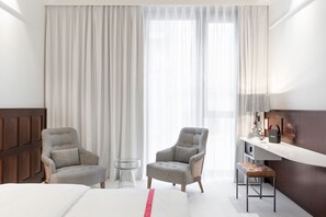 Una habitación de hotel con una cama, dos sillones, una mesita y un escritorio con lámpara.
