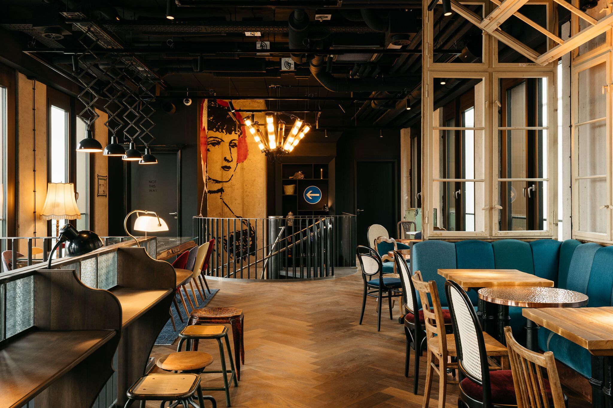 A restaurant interior with wooden tables, chairs, a bar area, and a mural on the wall.