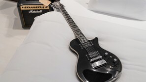 A black electric guitar on a bed with a Marshall amplifier box in the background. - Ruby Louise Hotel Frankfurt by IHG (Frankfurt)