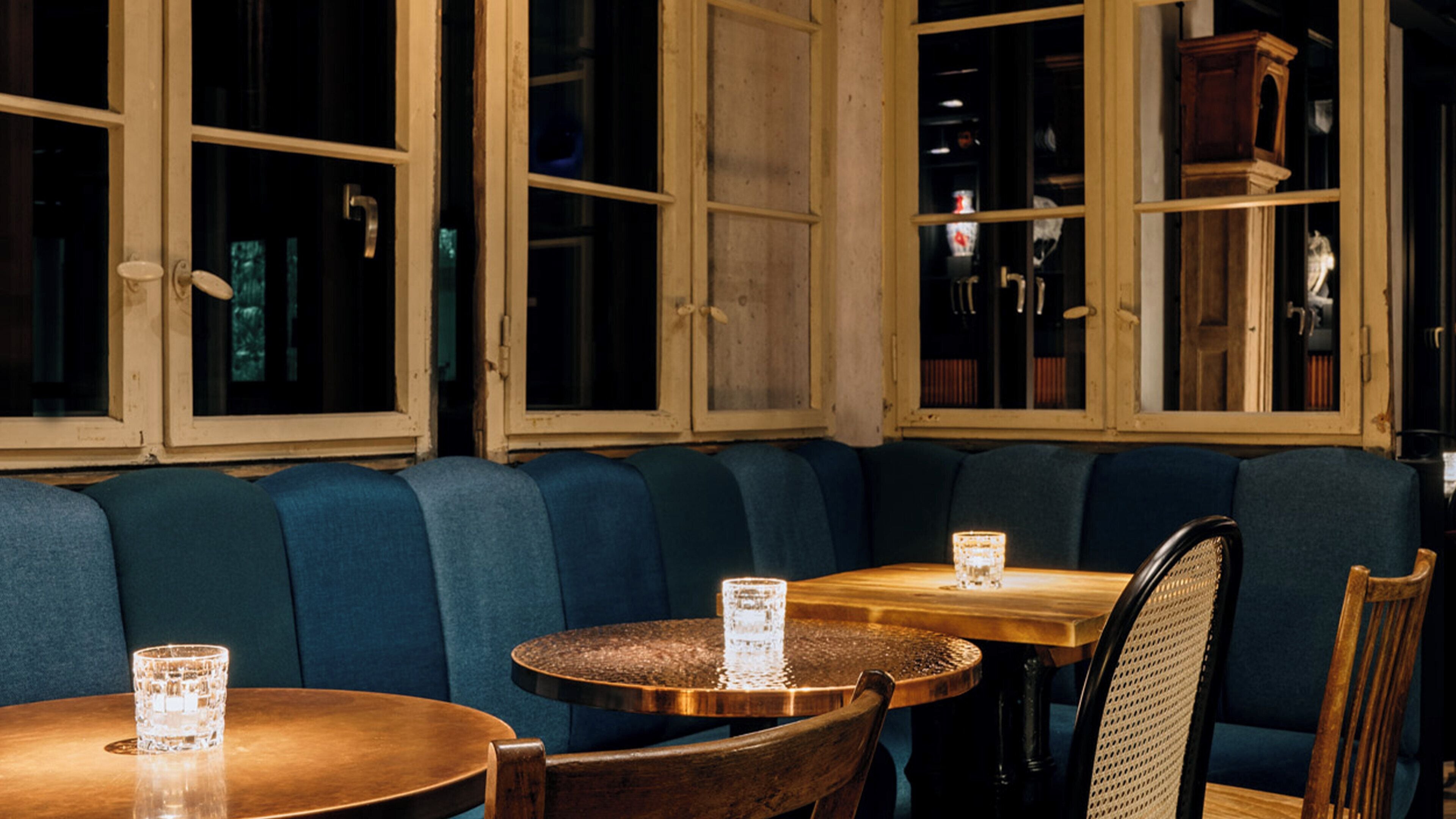 A restaurant interior with a booth seating area, round tables, and a wooden cabinet.