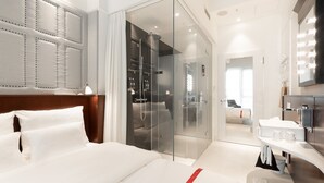 Et moderne hotelværelse med en stor seng, et glasindrammet walk-in-closet, et badeværelse med et toiletbord og et stort spejl.