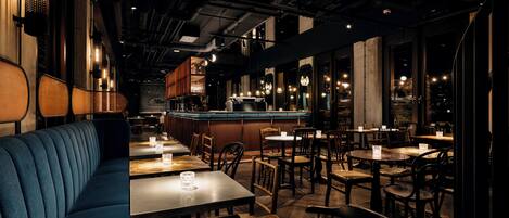 Interior de un restaurante con barra, distribución de mesas y vistas a través de las ventanas.